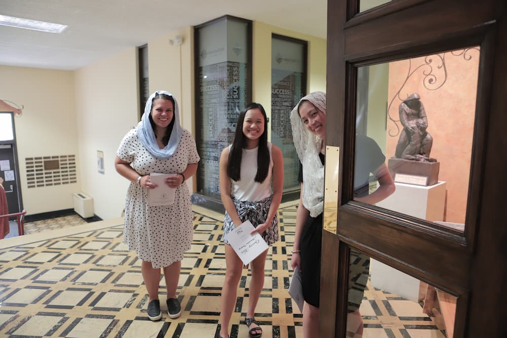 Three students wearing veils stand outside of St. John's Chapel.