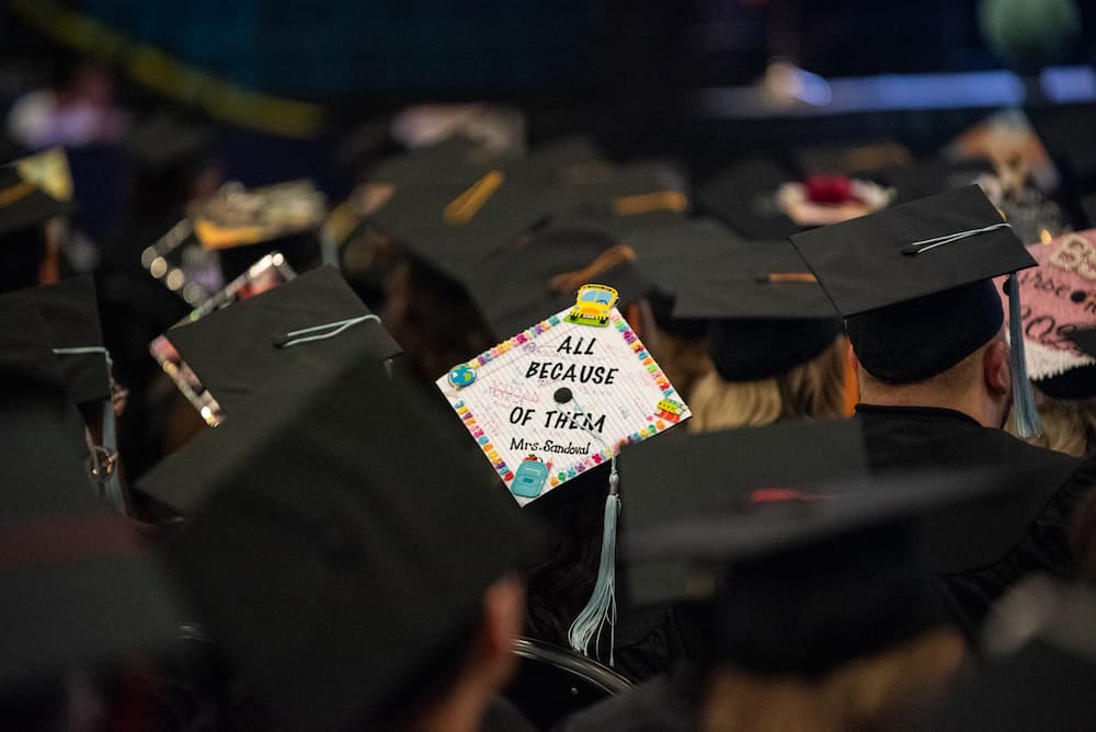 A graduation cap reads "All because of them."