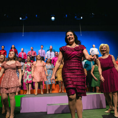 Deanne Zogleman stands in front of theatre cast.