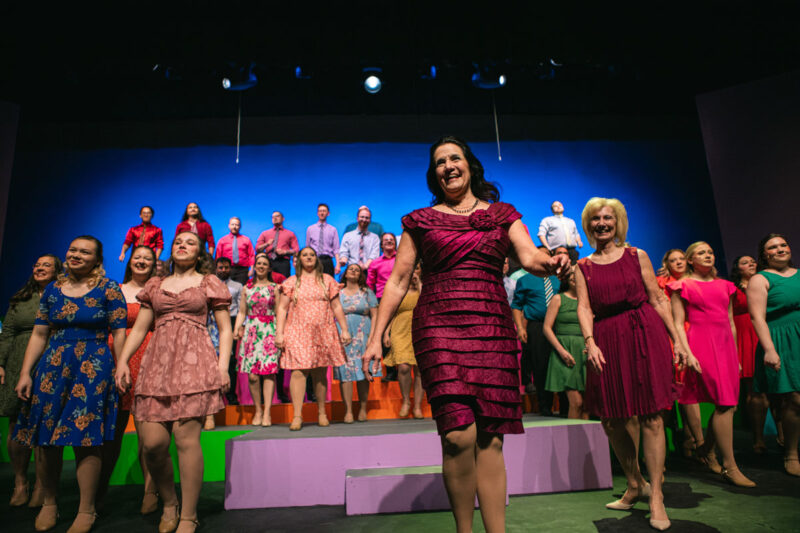 Deanne Zogleman stands in front of theatre cast.